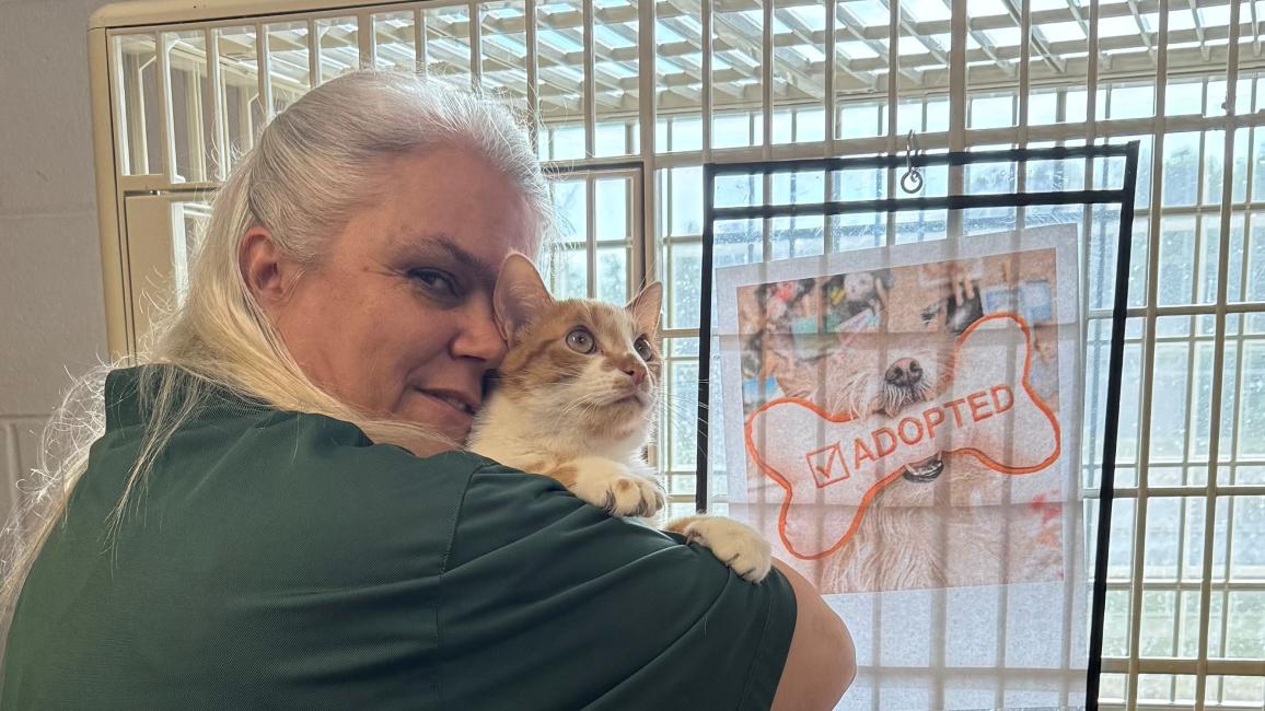 Renee Skipper holding a cat in front of a kennel
